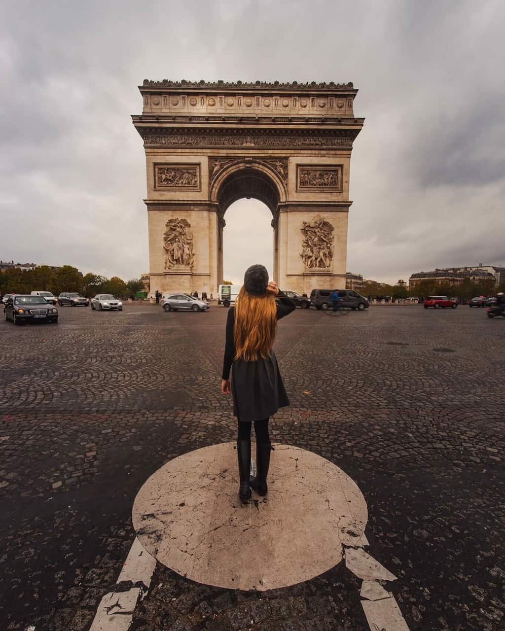 woman standing in black dress with long hair in front of the arc de triomph in paris