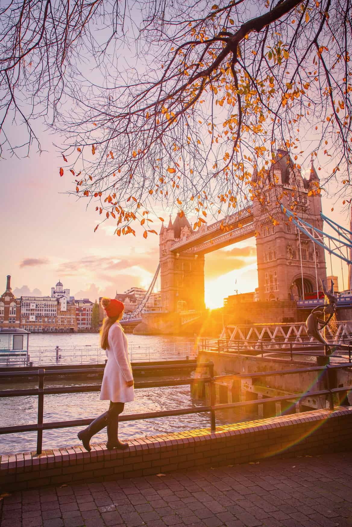 woman in white coat and red hat standing in front of tower bridge in london at sunset