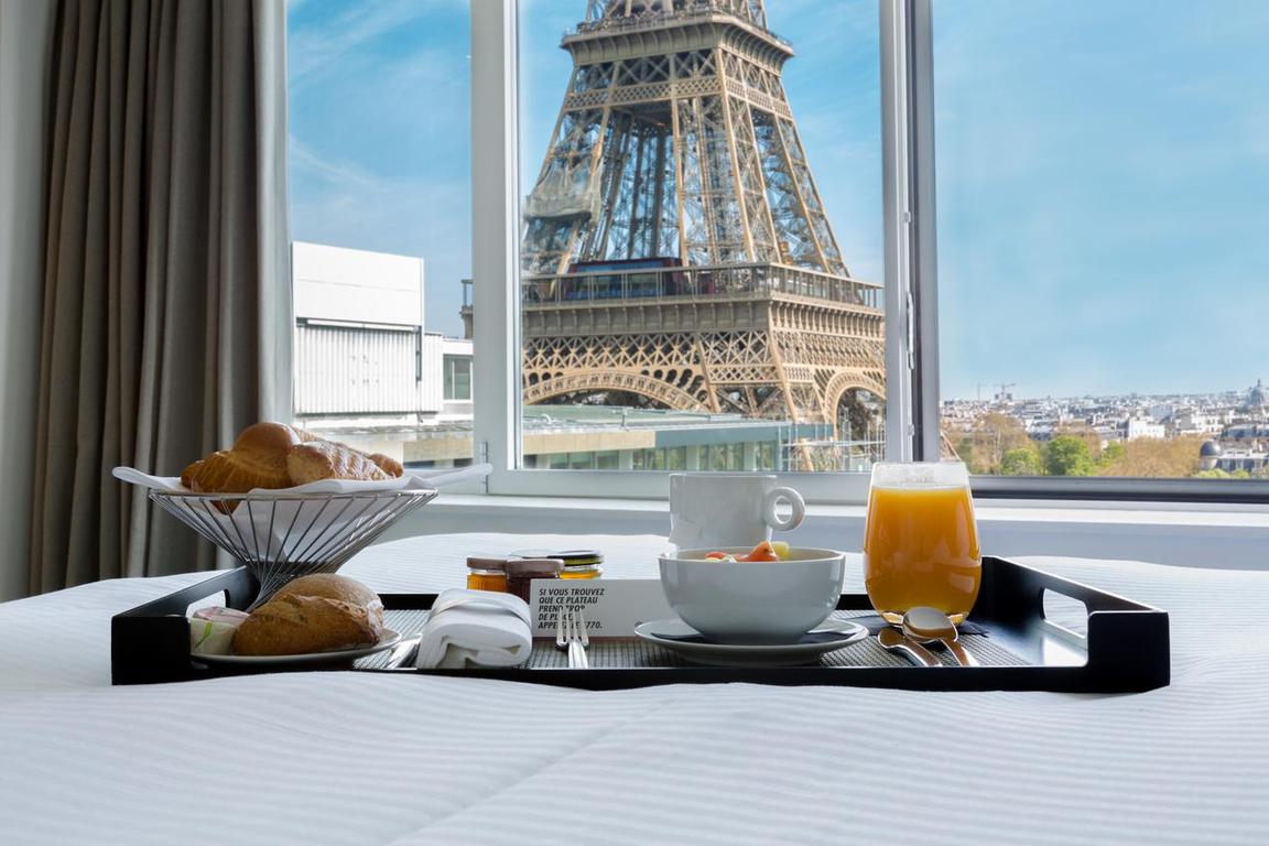 This gorgeous hotel, the Pullman, is known for it's iconic views of the Eiffel Tower! Photo of a heavily laden French breakfast tray sitting on a bed with a view of the base of the Eiffel Tower.