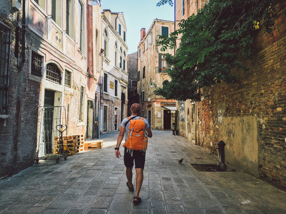 a man carrying a yellow backpack as he walks along cobblestone street