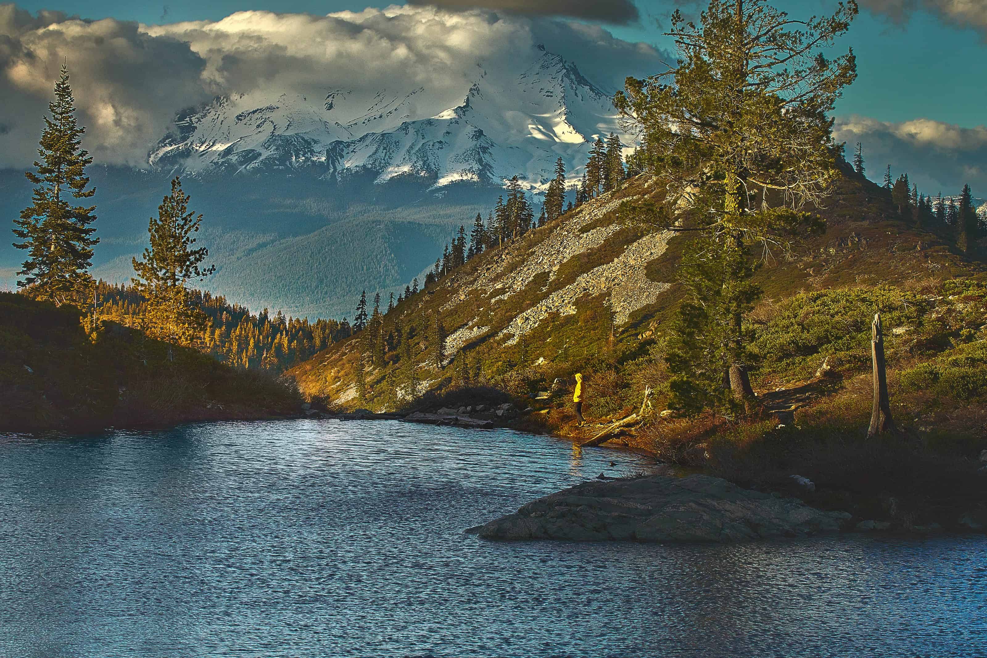 Figure in yellow standing on the edge of Heart Lake with Mount Shasta in the background.