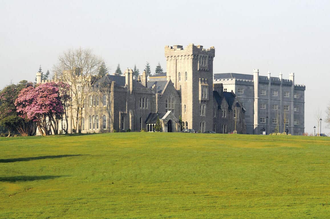 The stately Kilronan Castle sitting on a green field surrounded by flowering trees. This is one of the best castle hotels in Ireland!