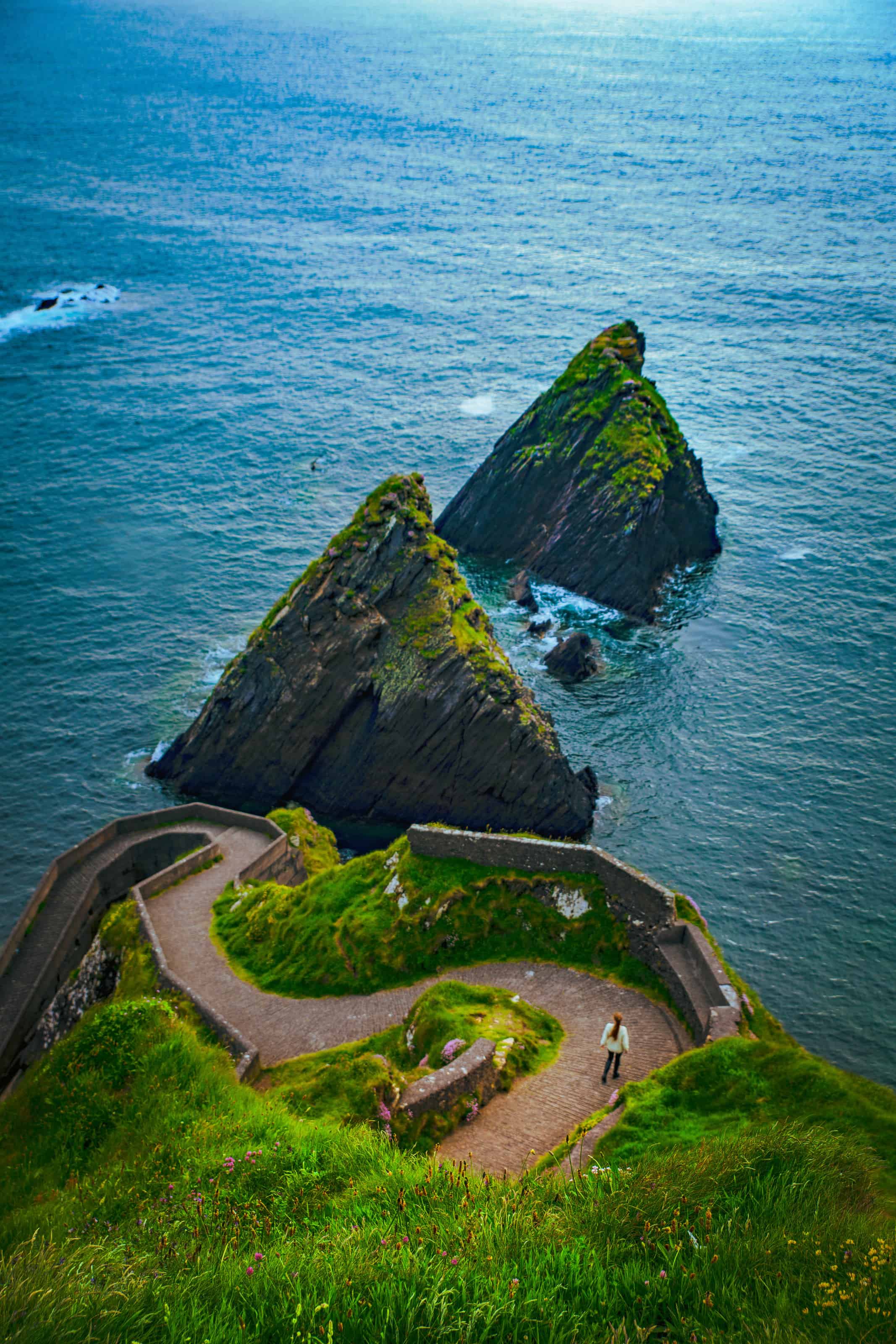 Woman walking the stone path at Dunquin Pier. with rugged rocks in the ocean.