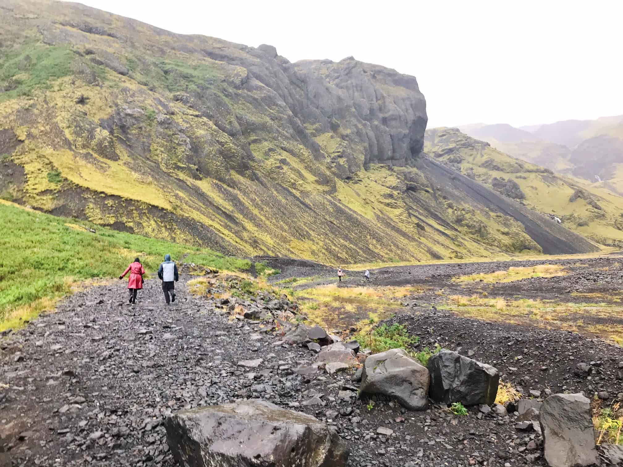 people on a trail with mountains in the background hiking to Seljavallalaug pool