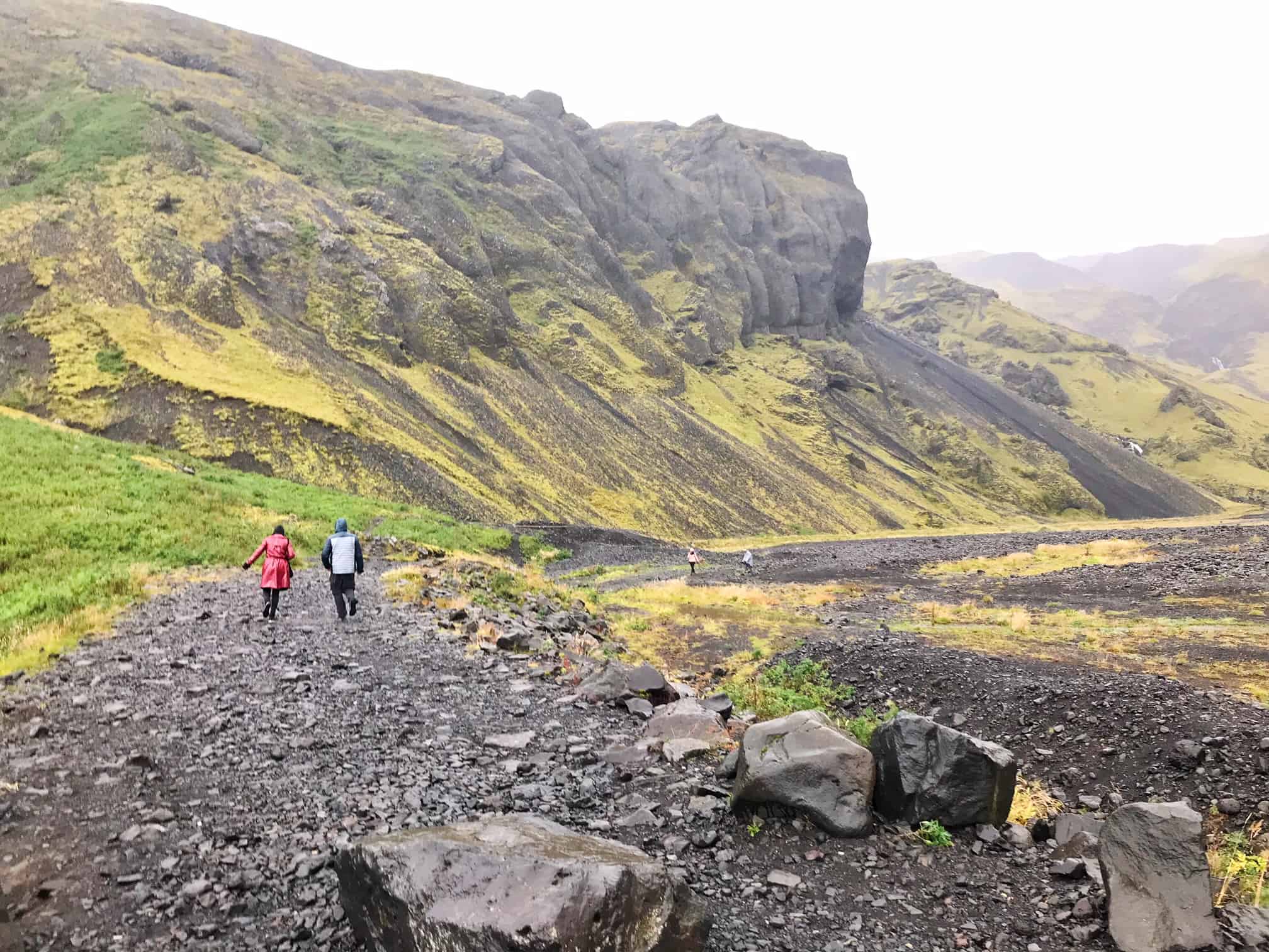 people on a trail with mountains in the background hiking to Seljavallalaug pool 