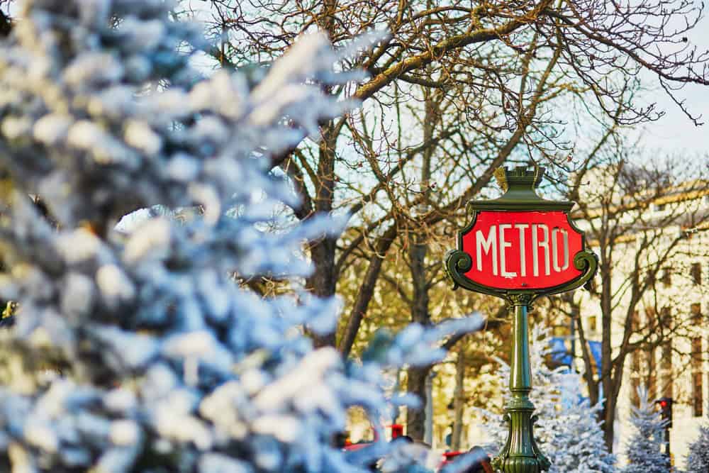 A Paris metro sign with nearby trees covered in snow.