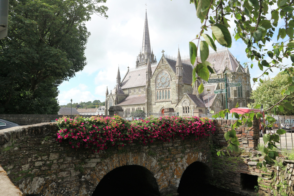 View of a stone bridge decorated with flowers and a gothic Cathedral in the distance in Clonakilty Ireland 