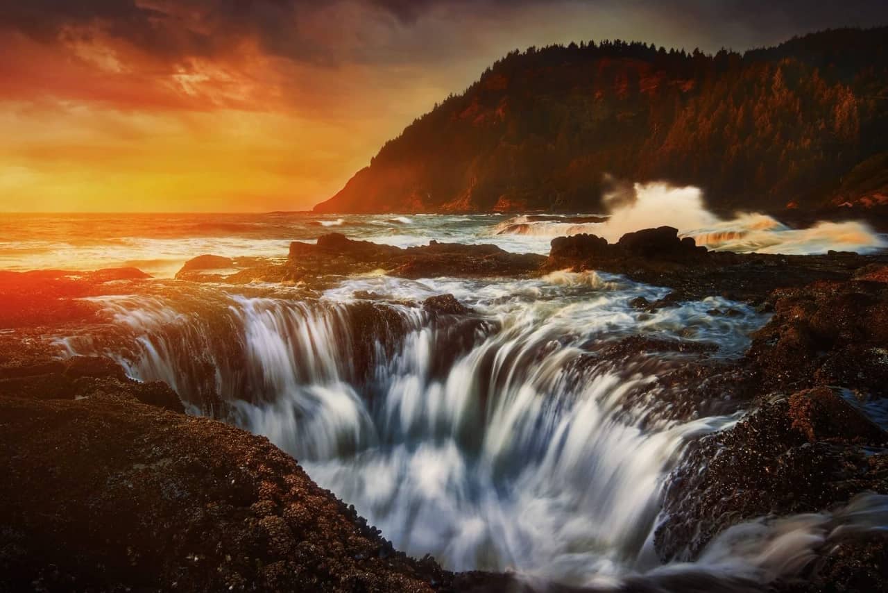 Water flowing into Thor's Well on the coast during an orange sunset.