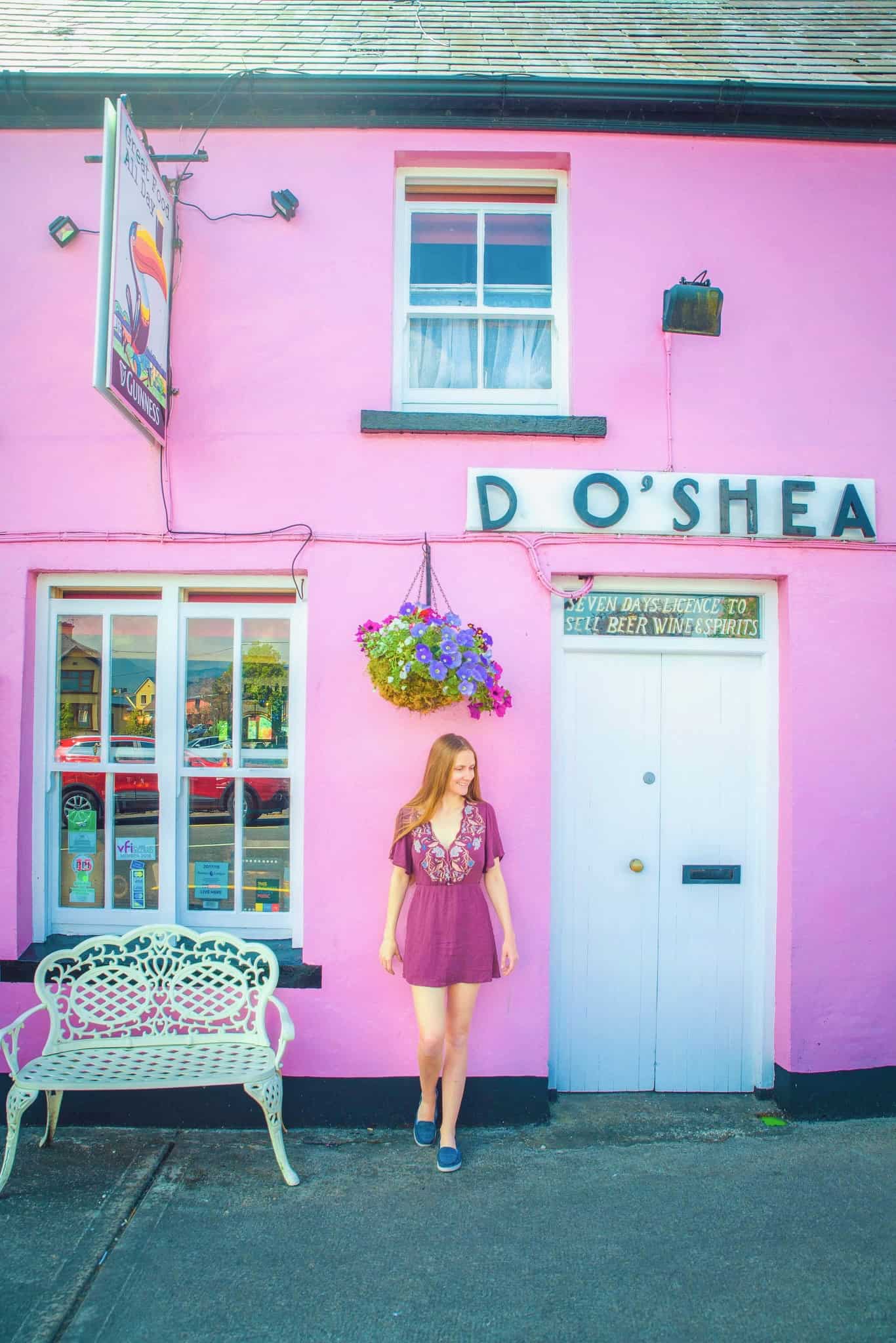 Victoria in a pink dress in front of a cute pink vintage building in Sneem, one of the cutest small towns in Ireland