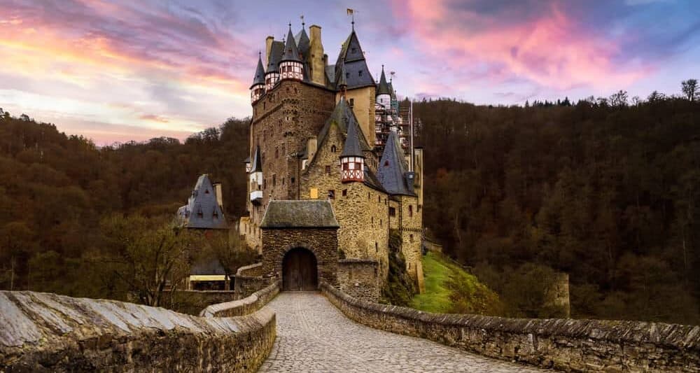 One of the most iconic castles in Germany, Burg Eltz sitting on a hill with its long walkway and purple cloudy sunset