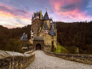 One of the most iconic castles in Germany, Burg Eltz sitting on a hill with its long walkway and purple cloudy sunset