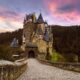 One of the most iconic castles in Germany, Burg Eltz sitting on a hill with its long walkway and purple cloudy sunset
