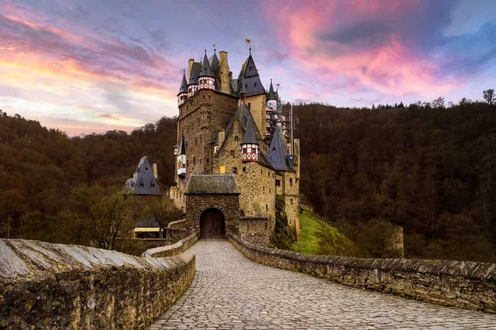 One of the most iconic castles in Germany, Burg Eltz sitting on a hill with its long walkway and purple cloudy sunset