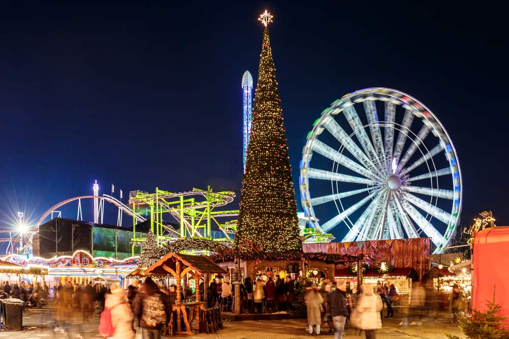 London Christmas Market with tall Christmas tree, Ferris wheel, and stalls at night.