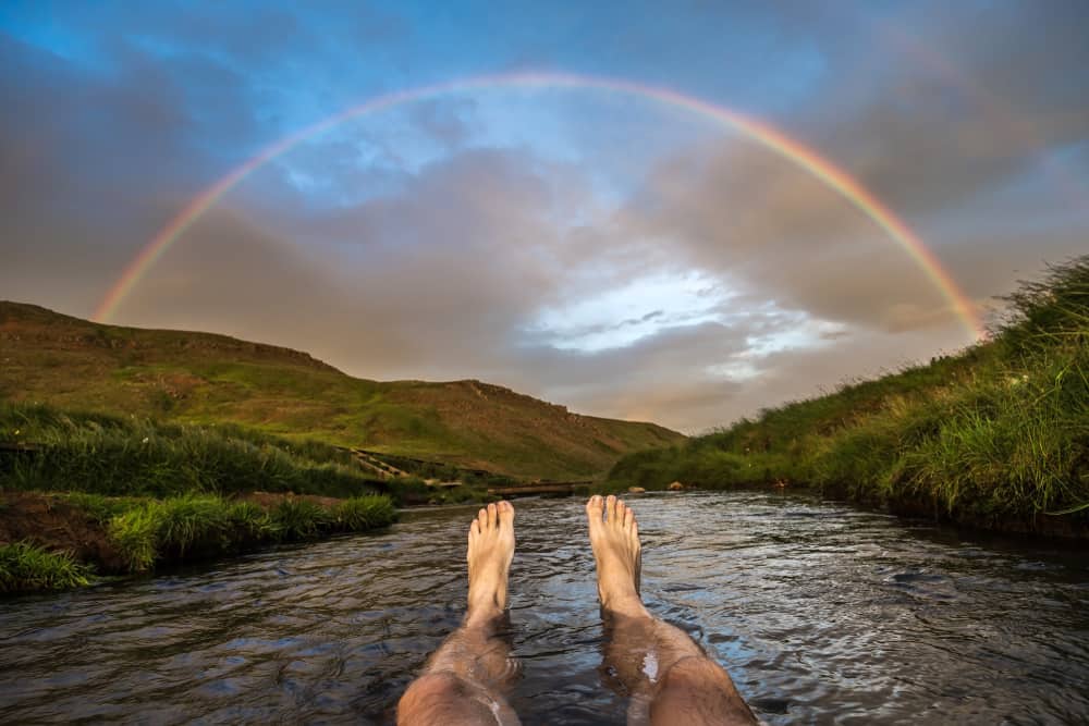 person looking at rainbow while bathing at Reykjadalur Hot Springs 