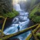 Man standing at the base of a rushing river with Koosah Falls in the background