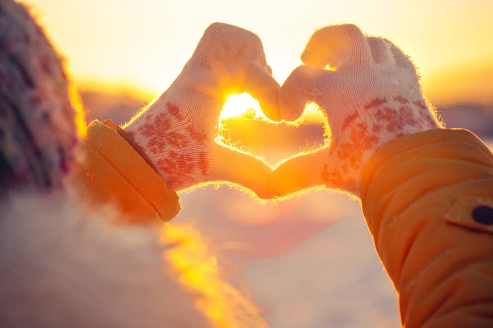 hands in winter making a heart with sun