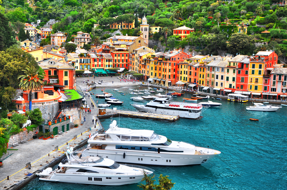 Yachts and small boats in a harbor in Portofino, Italy, with colorful buildings in the background.