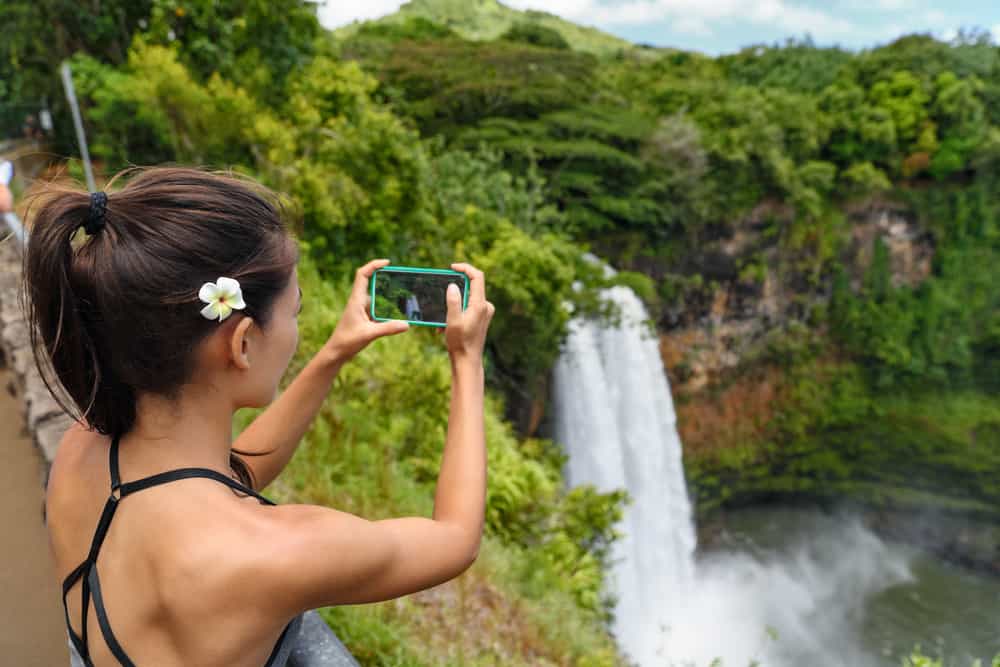 Don't forget a phone charger when planning your Hawaii packing list so you can take photos of waterfalls like this woman is! 