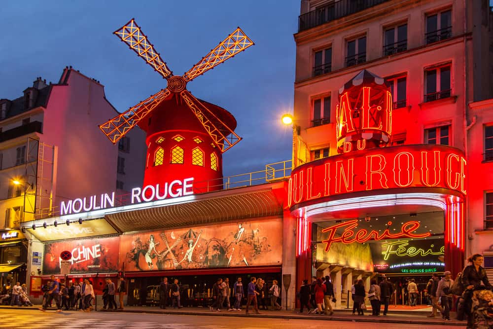 Moulin Rouge with the windmill lit in red light at night, Paris in a Day