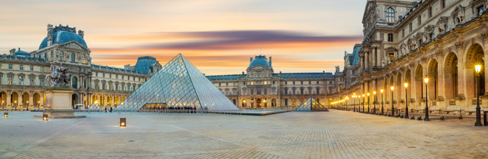 The Louvre and the Pyramid installation set against a light sunset sky