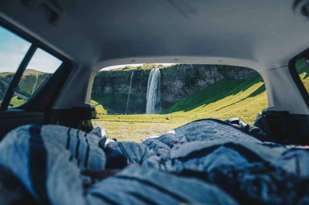 people camping in their car rental in iceland by a waterfall