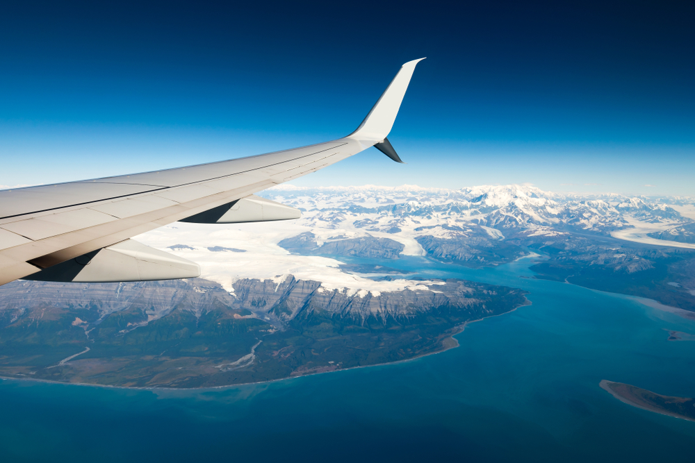 View out the plane window with the wing and snowcapped mountains below.
