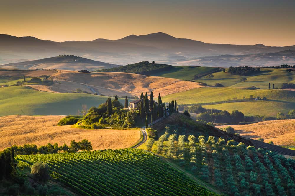 Aerial views of the rolling hills of Val d'Orcia with a villa at golden hour.