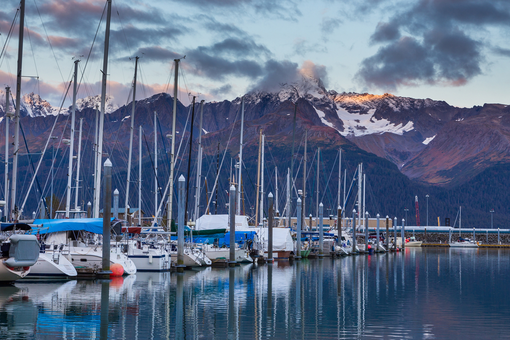 Dusk falls over the sailboats in the Seward marina with purple mountains in the distance.