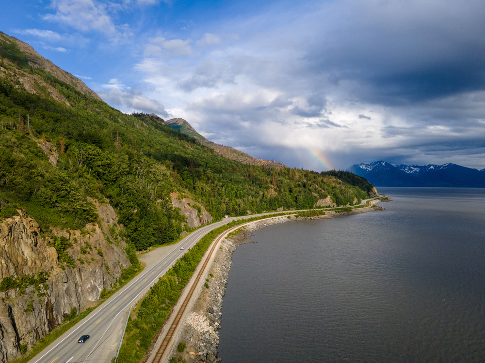 Aerial view of the Turnagain Arm Highway with mountians on one side and water on the other, one of the best drives on your Alaska road trip.