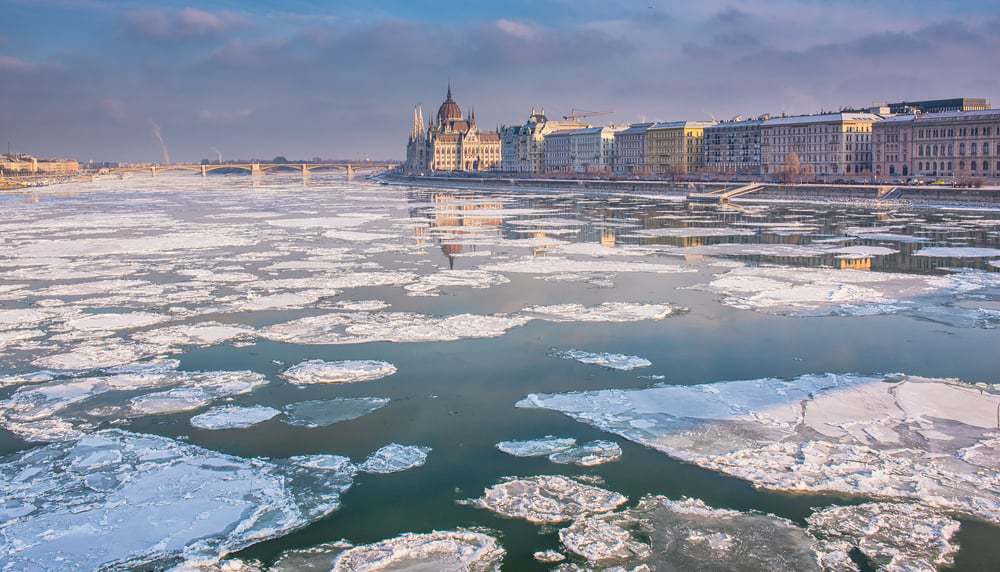 sheets of ice over the Danube river with buildings in the city of budapest in the background
