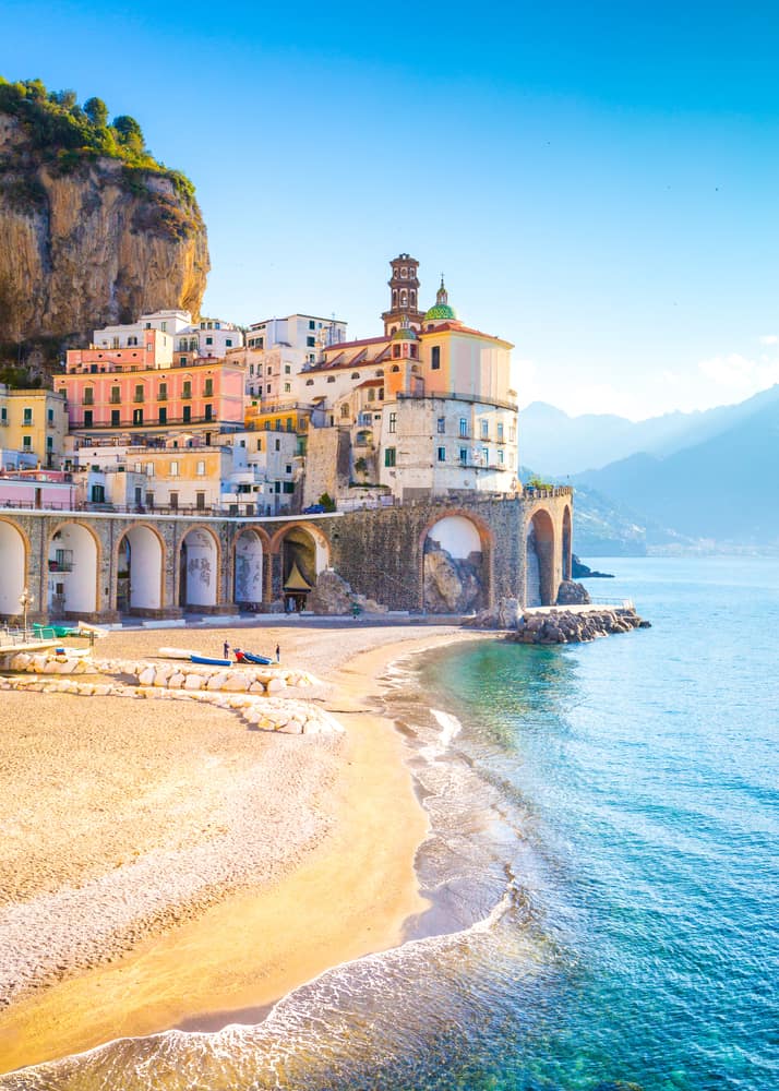 A beach on the Amalfi Coast with a viaduct and mountains in the background.