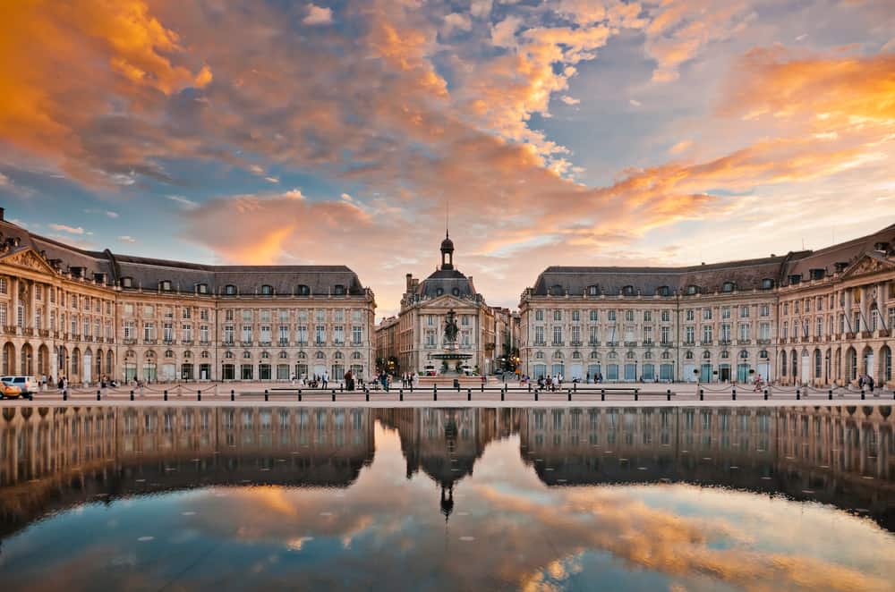 Vivid sunset over Place de la Bourse reflecting in a large pool in a square.