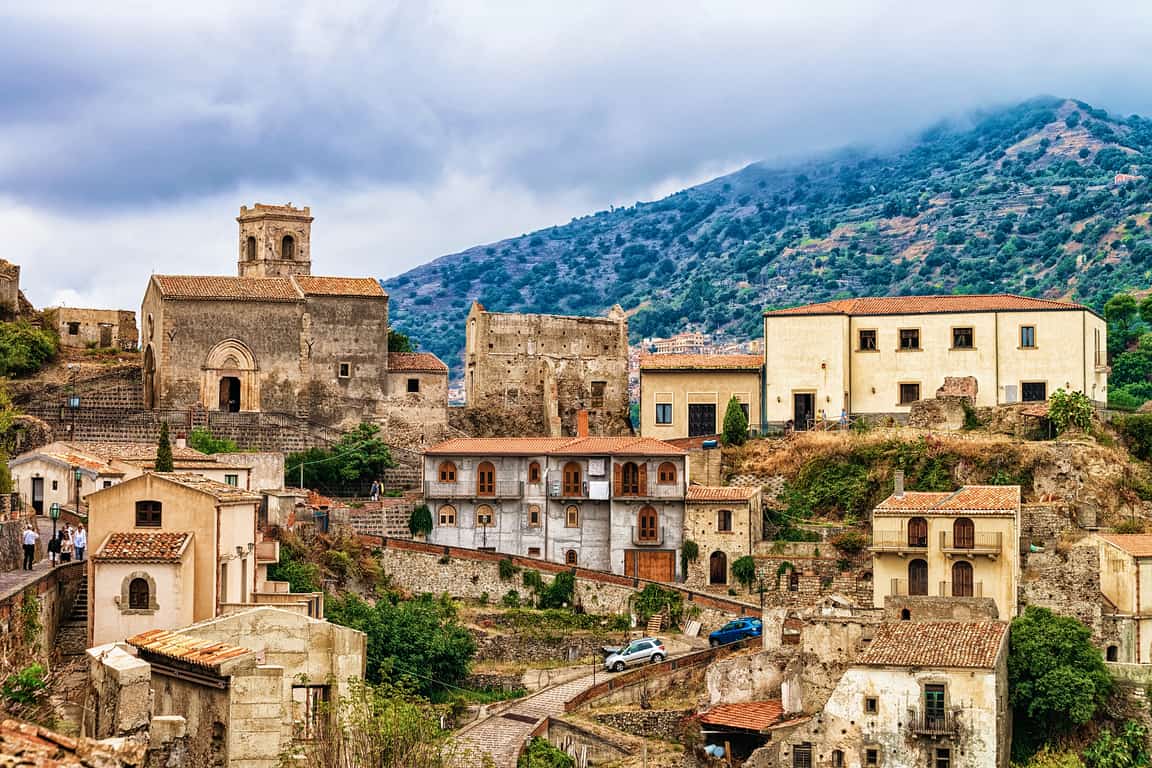 Historic, stone buildings stacked on hills in Savoca on a cloudy day.