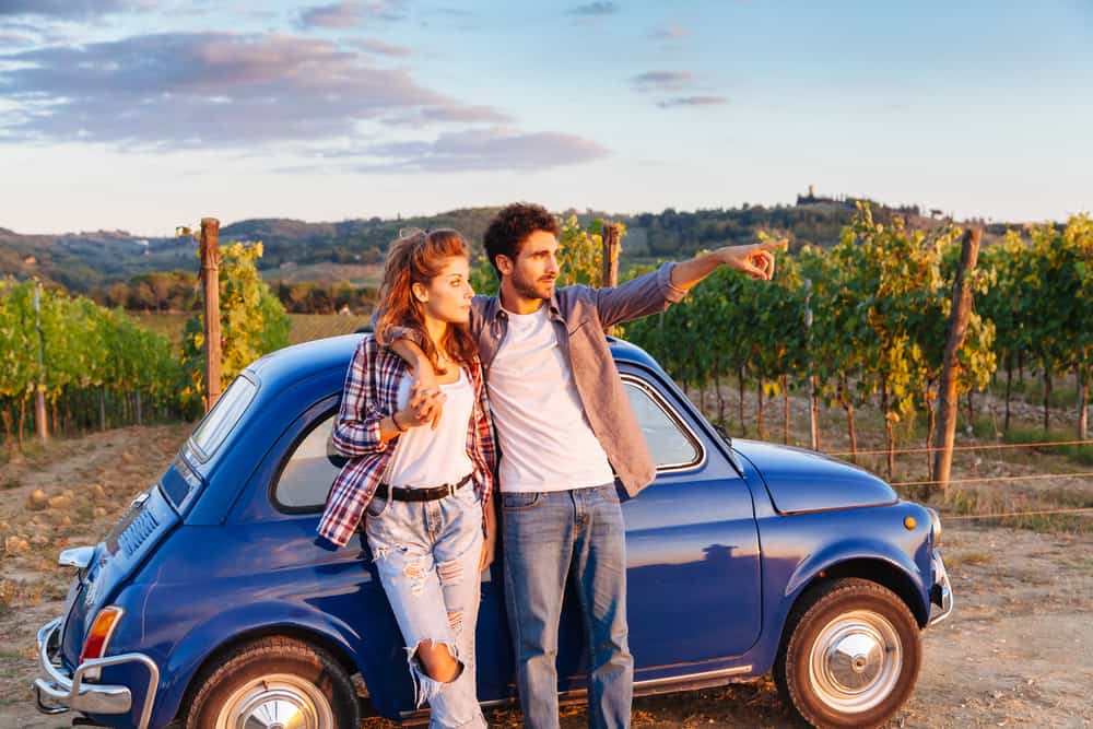 Photo of couple with a car in Italy, an excellent way to travel during your Tuscany honeymoon.