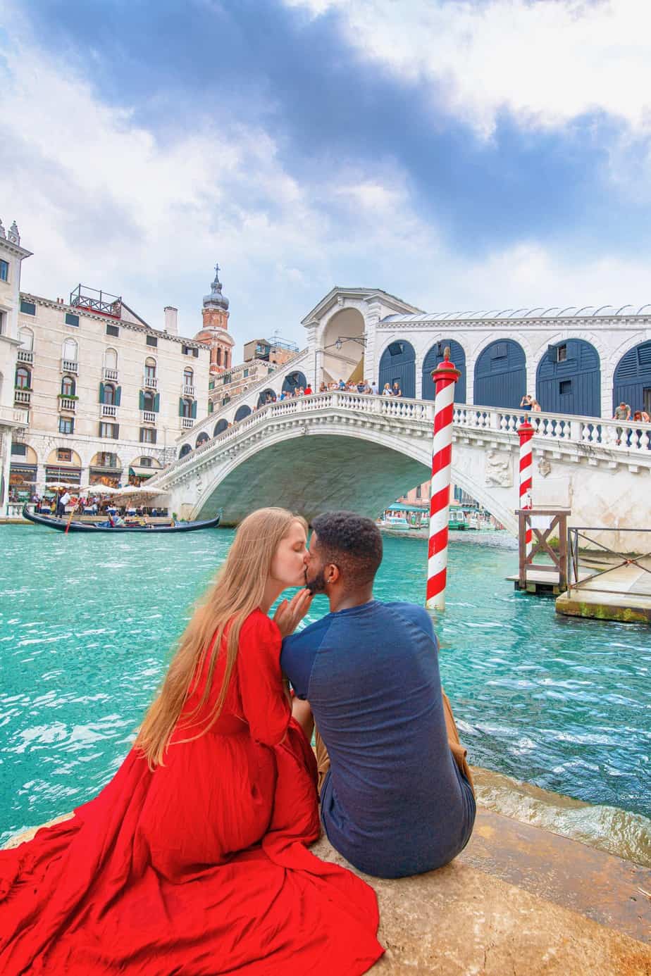 Cute couple sitting and kissing in front of the Rialto Bridge in Venice, Italy.