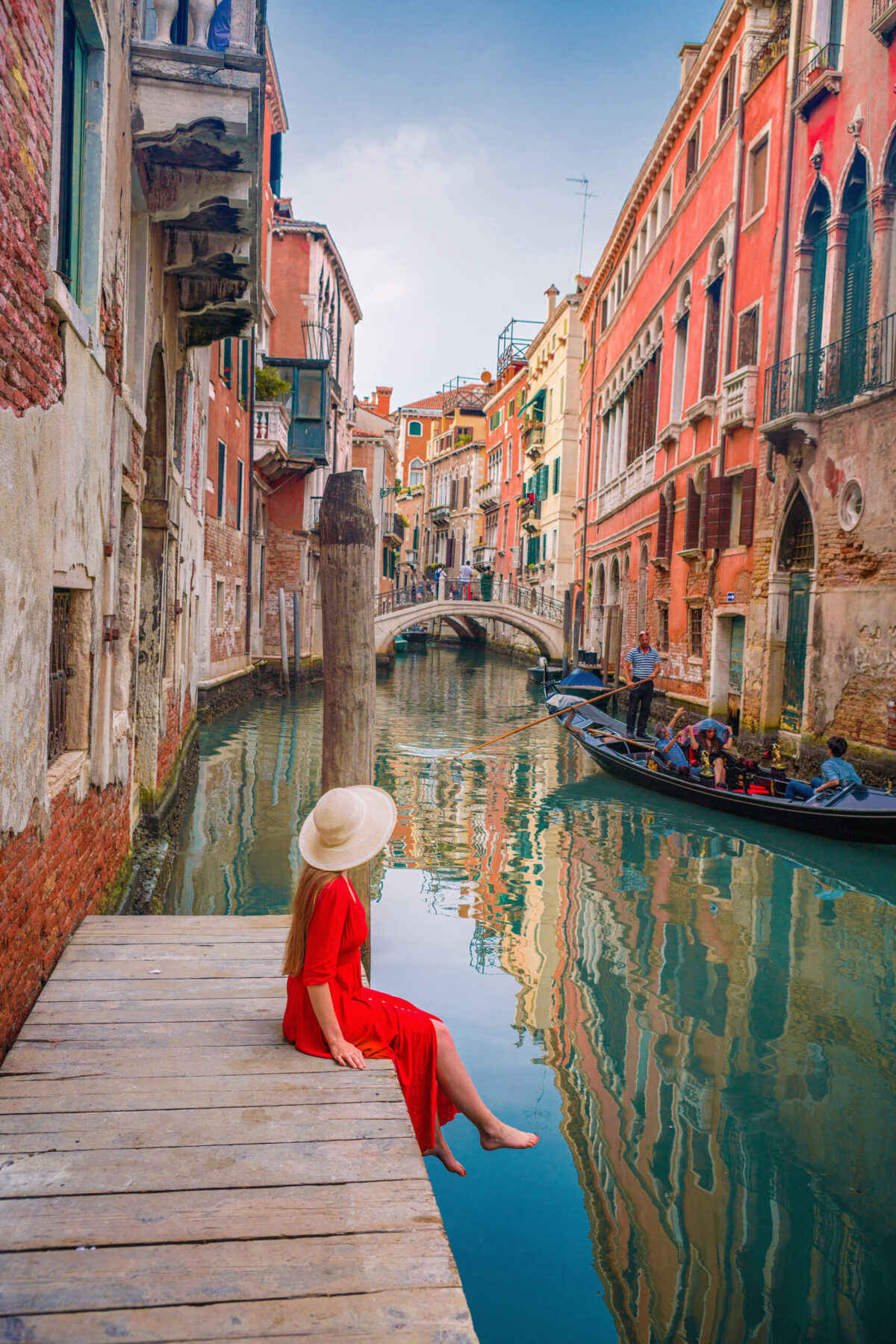 woman in red dress sitting on dock in Venice with gondola on a canal.