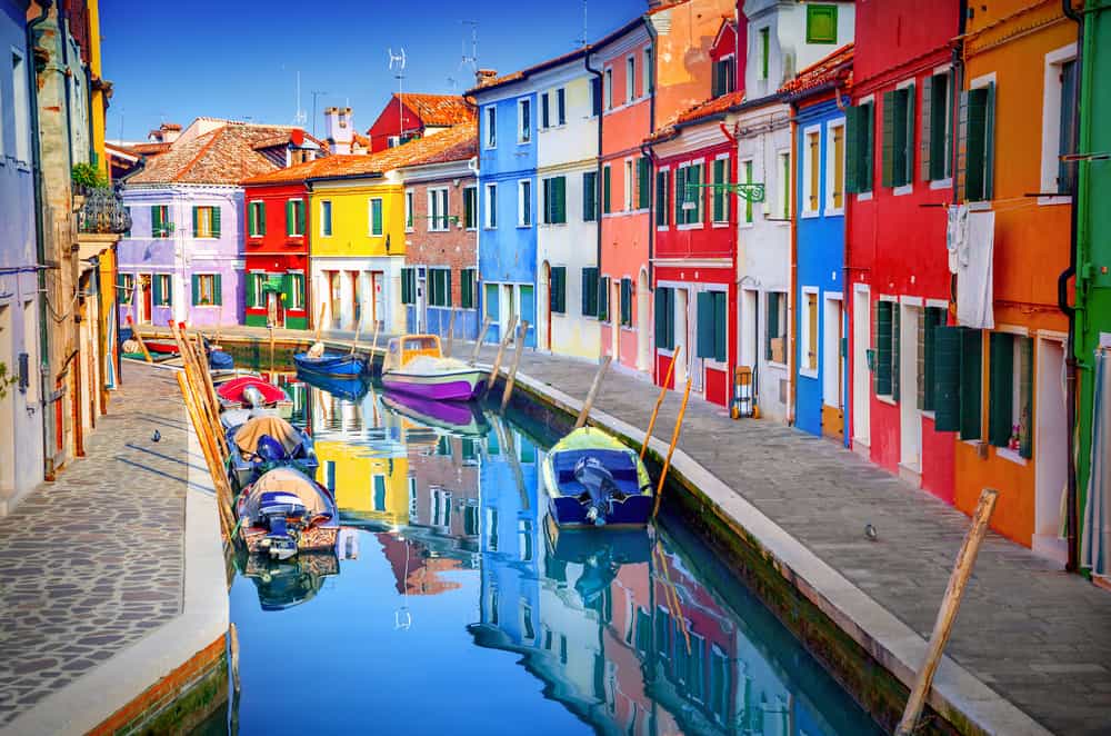 Colorful, bright buildings in Burano with a canal filled with colorful boats.