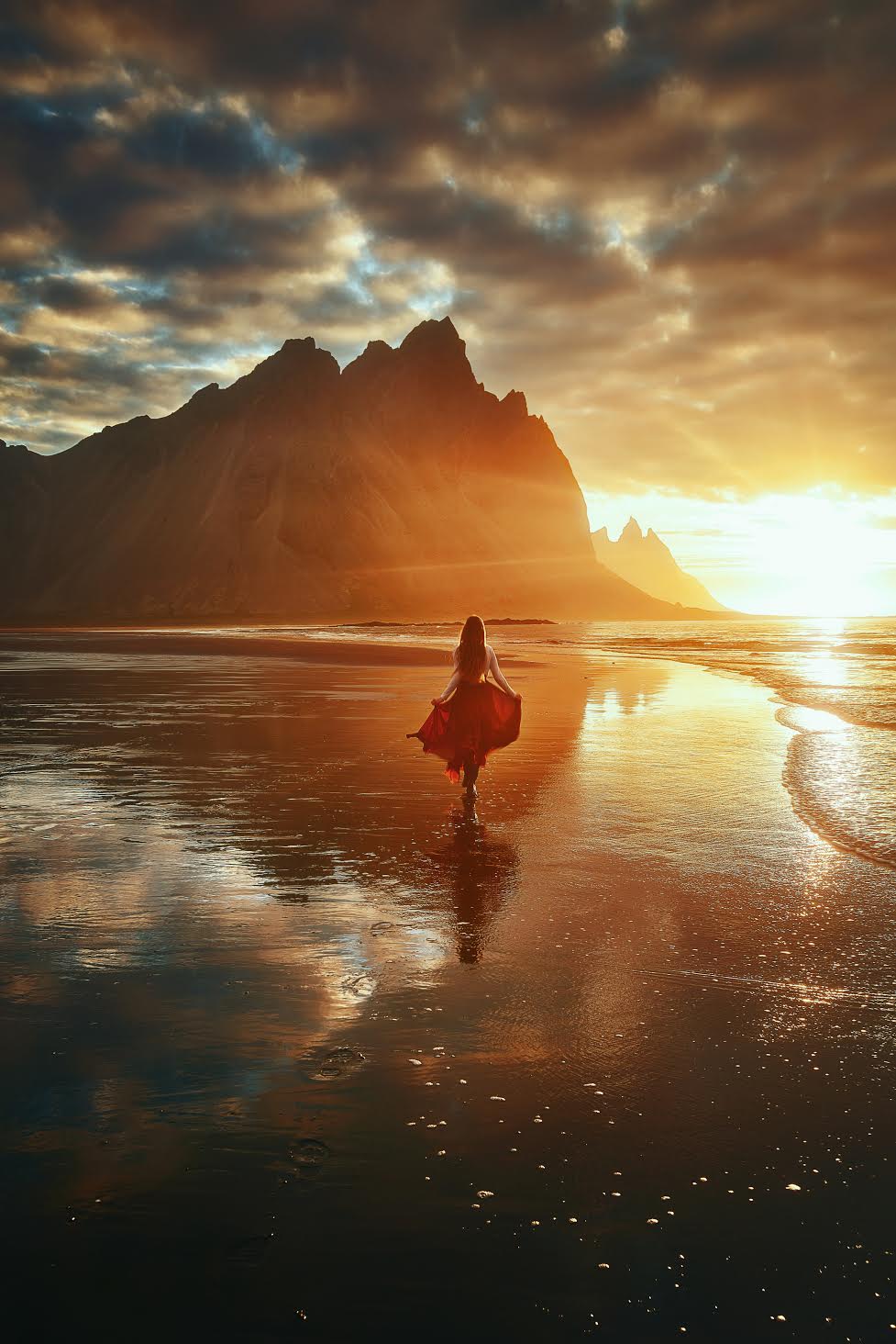 woman in red skirt running toward sunrise on Vestrahorn at Stokksnes Peninsula 