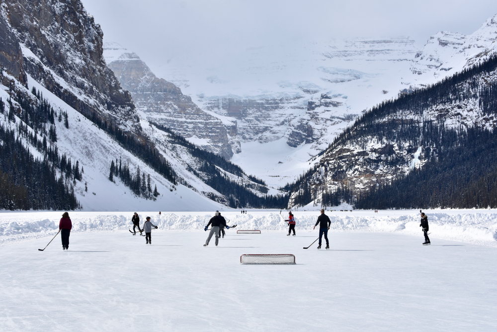 People playing ice hockey on the frozen Lake Louise with mountains in the background.