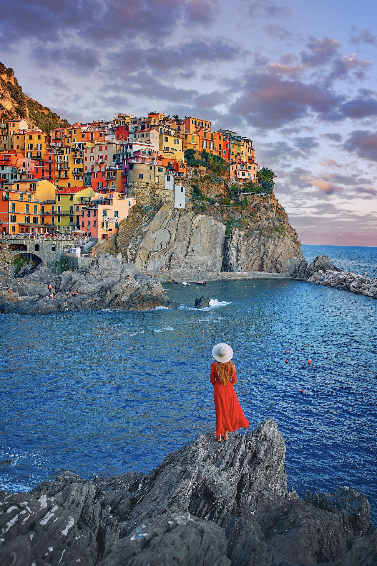 woman standing on the rocks in front of the water and colorful buildings of Cinque Terre during a Northern Italy itinerary.