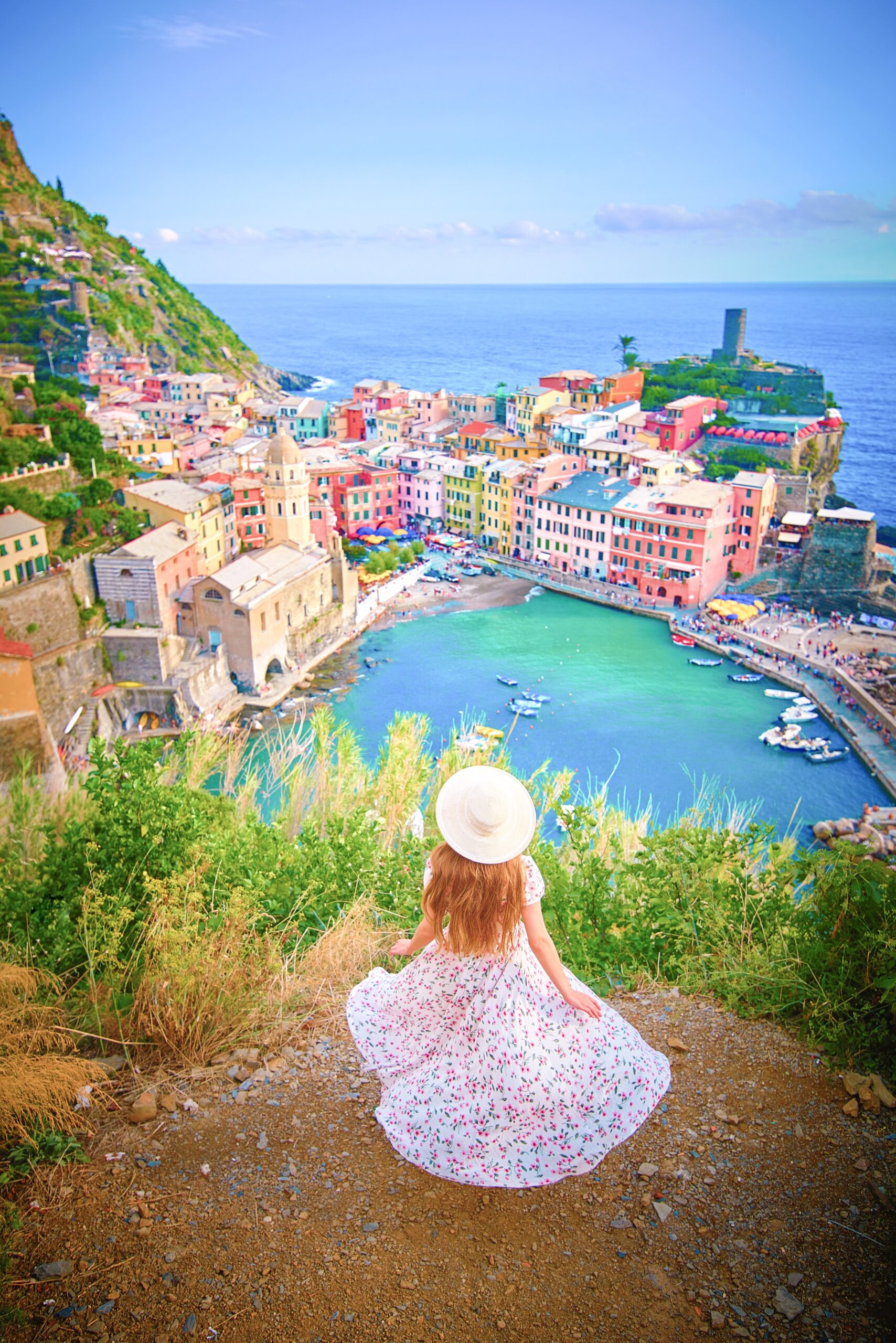 woman in flowery dress in front of teal waters and colorful buildings of Cinque Terre on a Northern Italy itinerary