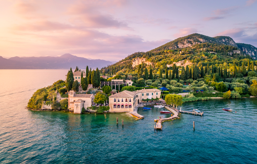 Aerial view of a beautiful villa on Lake Garda with green mountain, blue waters, and colorful sky