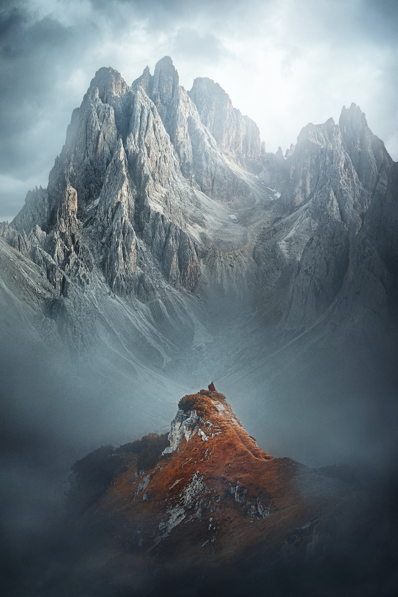 gray towering mountains with tiny woman in red cape in the forefront on a Northern Italy itinerary