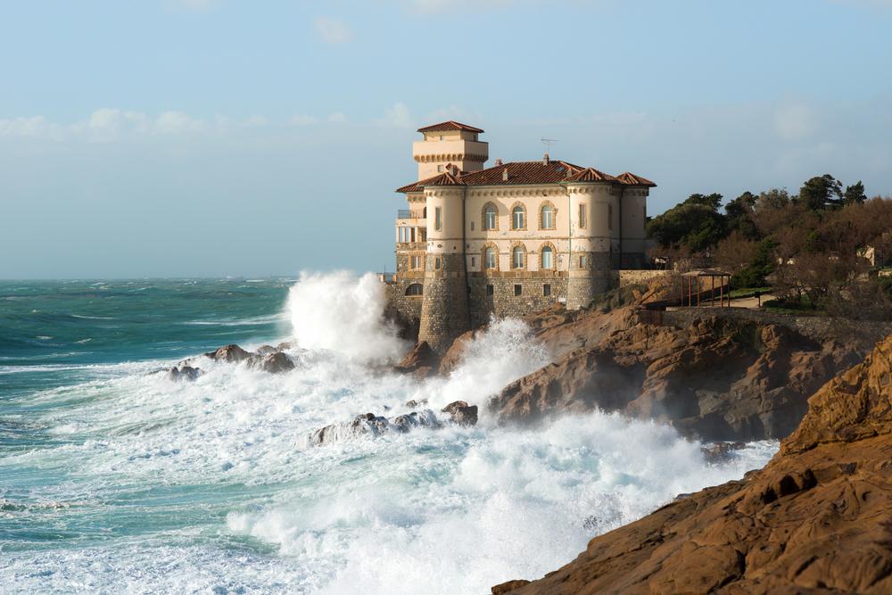 Ocean waves crashing into the rugged shore with Boccale Castle in Tuscany.