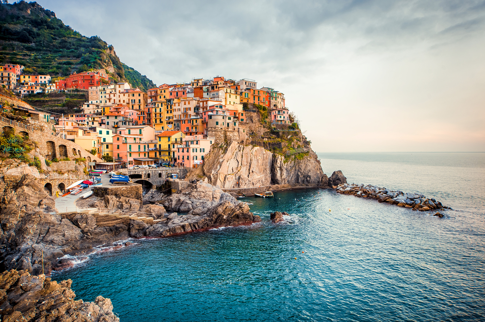 Colorful buildings of Cinque Terre viewed across the water on a cloudy day.