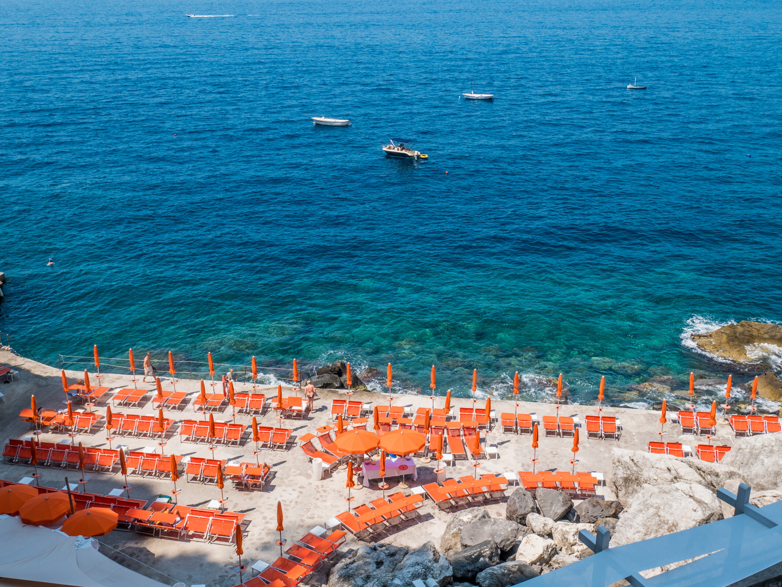 Photo of Gavitella Beach, one of the more secluded Amalfi Coast beaches. Orange colored umbrellas and bold blue water is pictured. 