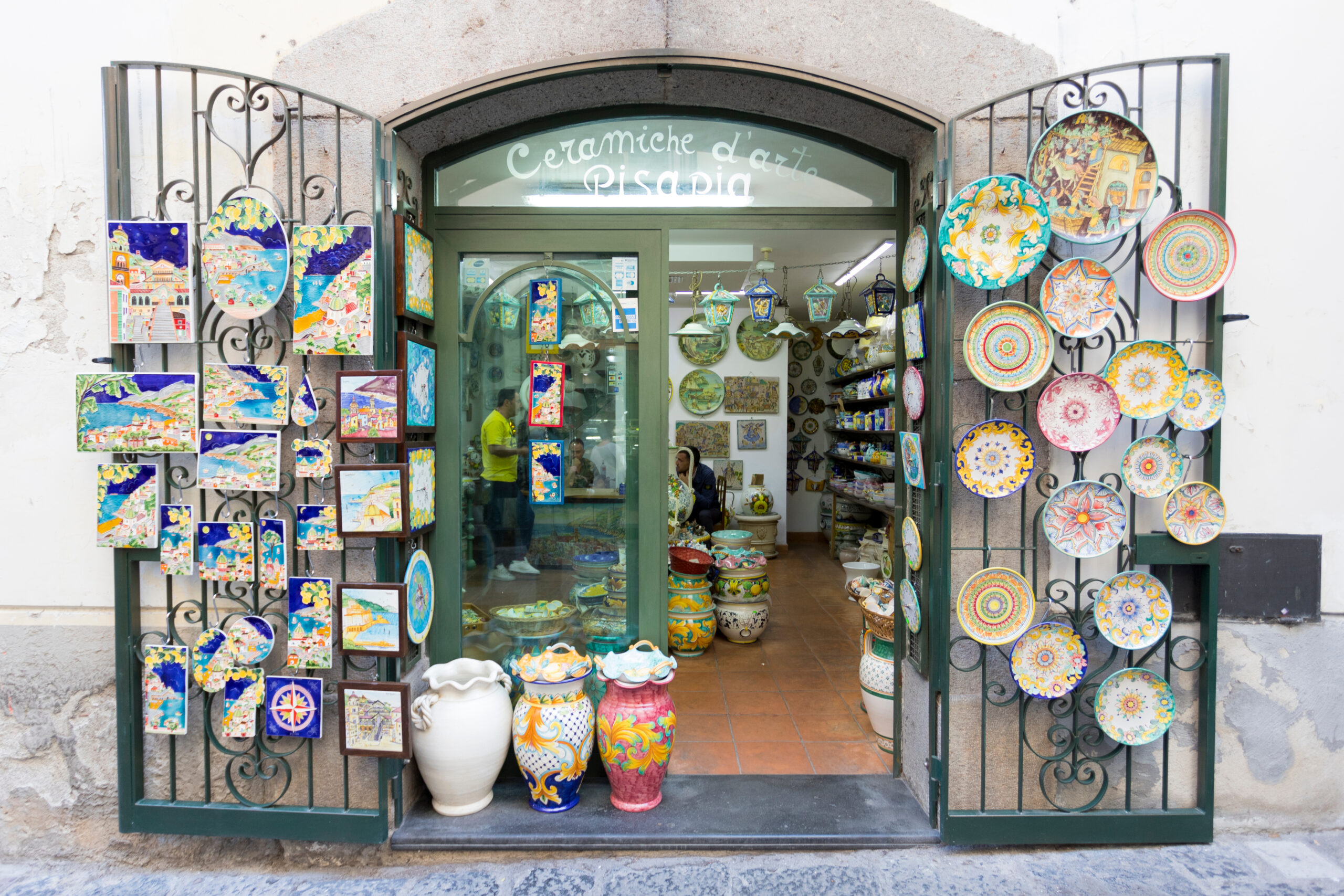Photo of majolica ceramics found in Vietri sul Mare, one of the best Amalfi Coast beaches for unique souvenirs. Plates, wall hangings, and vases are being displayed in a store front.