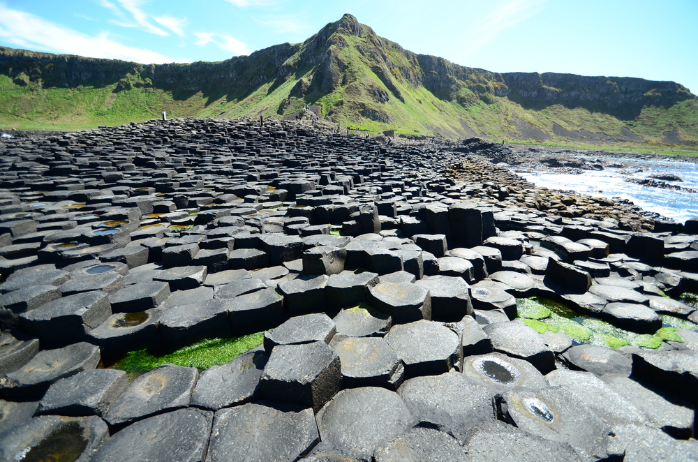 hexagonal black rock landscape in front of green mountain