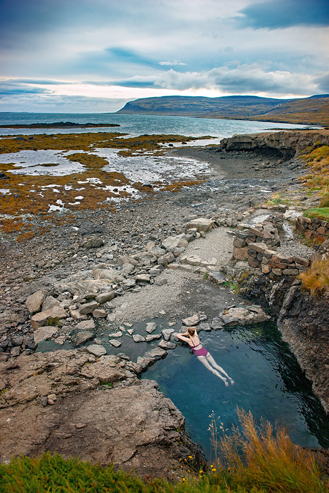 Woman laying in the secret Hellulaug hot spring in Iceland